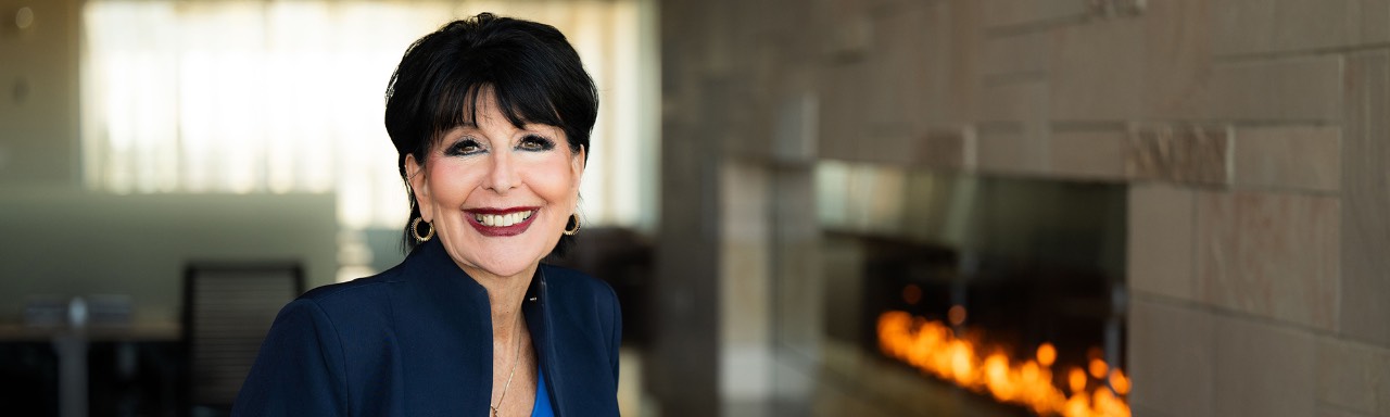 President Philomena Mantella portrait - she's posed in the Mary Idema Pew Library in front of a lit fireplace - she's smiling